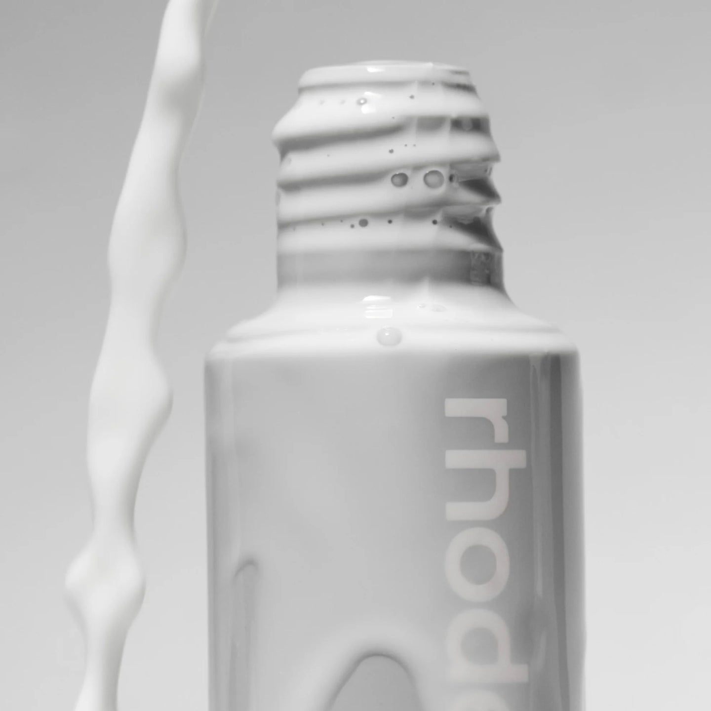 White bottle with 'rhode' branding on a gray background