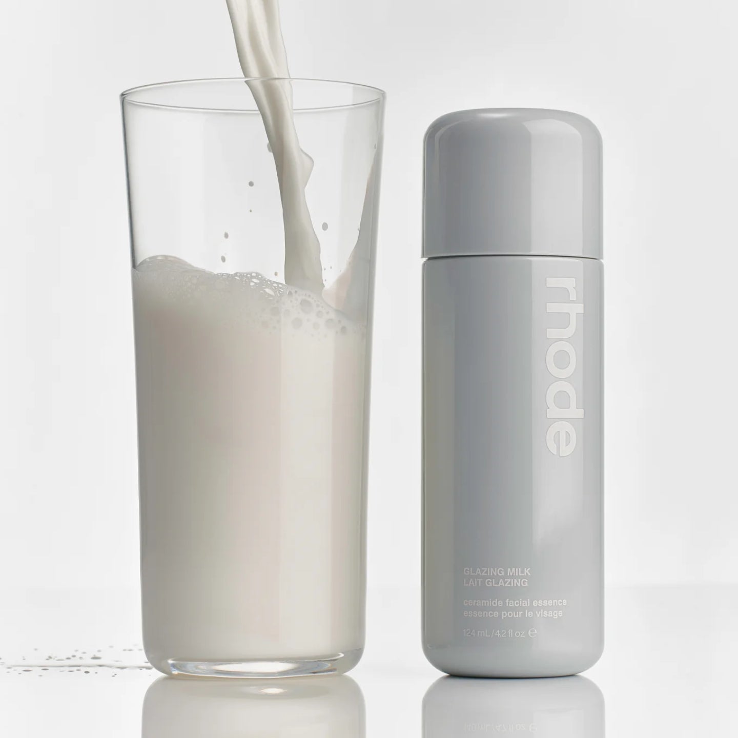 Glass of milk being poured next to a bottle labeled 'rhode' on a light gray background