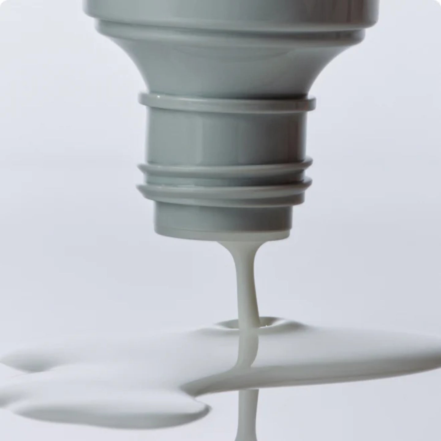 Close-up of a light bulb with white liquid dripping from it against a light gray background