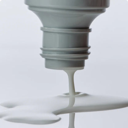 Close-up of a light bulb with white liquid dripping from it against a light gray background